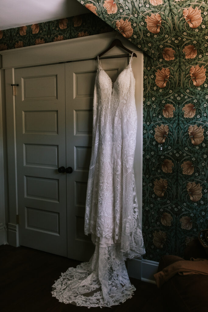 Wedding dress hanging inside the Marley House at Finley Farms wedding venue. There is white woodwork and green floral wallpaper.