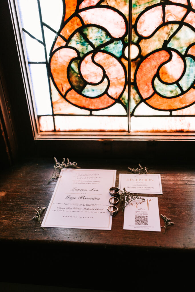 Wedding invitations and rings in the deep windowsill of a beautiful stained glass window. Part of a series of wedding detail shots by Missouri Wedding Photographer Bailey Morris.