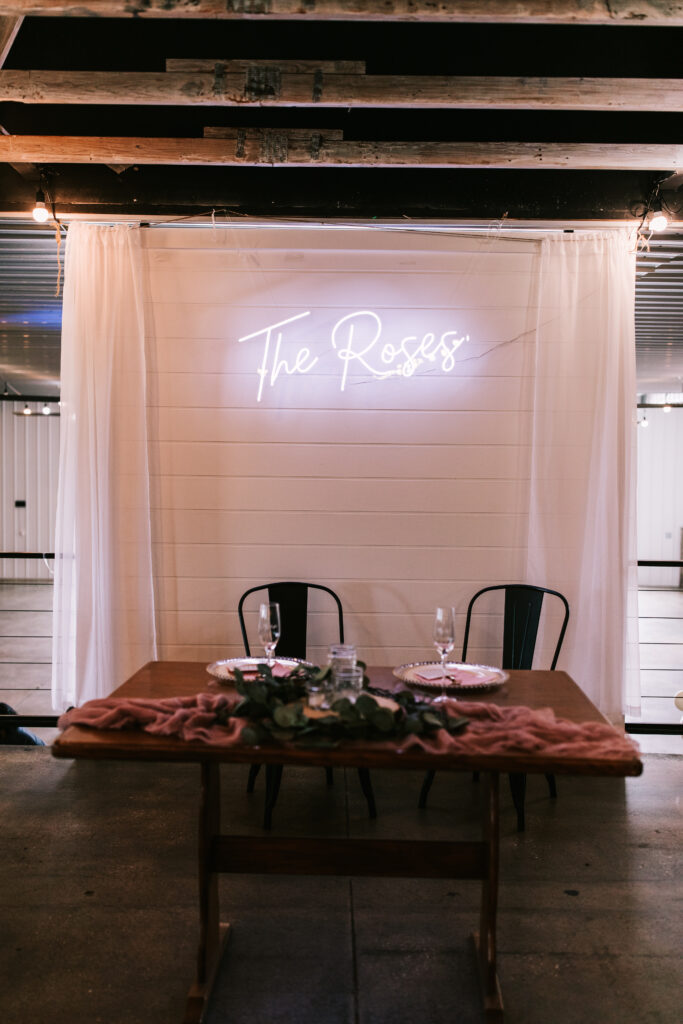 Sweetheart table set up in front of a neon sign that says The Roses at a wedding at The Atrium. Part of a series of wedding detail shots by Morris Wedding Photography. 