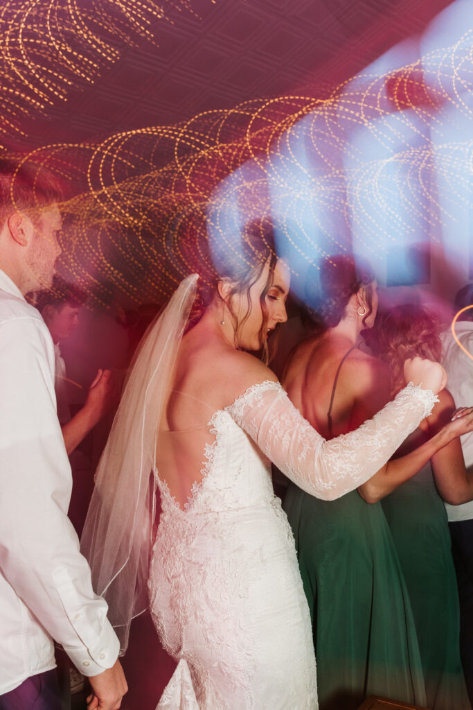 Bride line dances at her wedding reception with the lights making curves and blurs in the photo. 