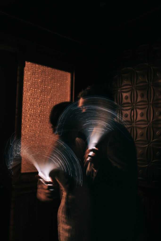 Bride and groom kiss in the dark reception hall while waving light wantds which creates the blurry wedding photo trend. 