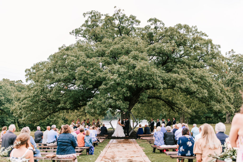 Magnificent oak tree is the backdrop for an outdoor wedding ceremony at Mighty Oak Lodge in Lebanon, Missouri. Wedding photography by Bailey Morris.
