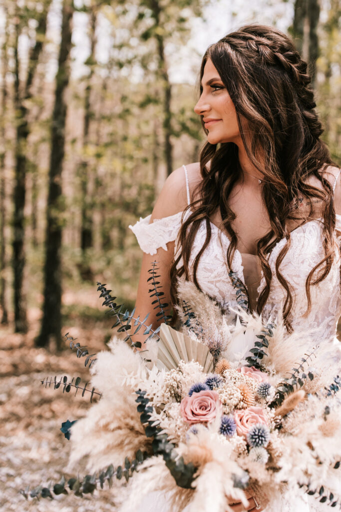 Bride gazing to the side holding a gorgeous bridal bouquet during a spring season wedding while standing in the woods photographed by Bailey Morris.
