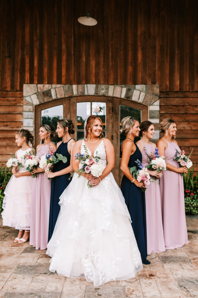 Bride with her bridesmaids in front of stone arch and wooden door in Lebanon Missouri. Photographer: Bailey Morris. 