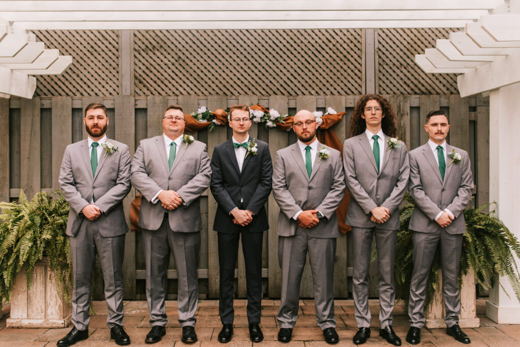 Groom and his groomsmen under a pergola wearing gray suits with green ties in Springfield, Missouri during a spring season wedding photographed by Bailey Morris.
