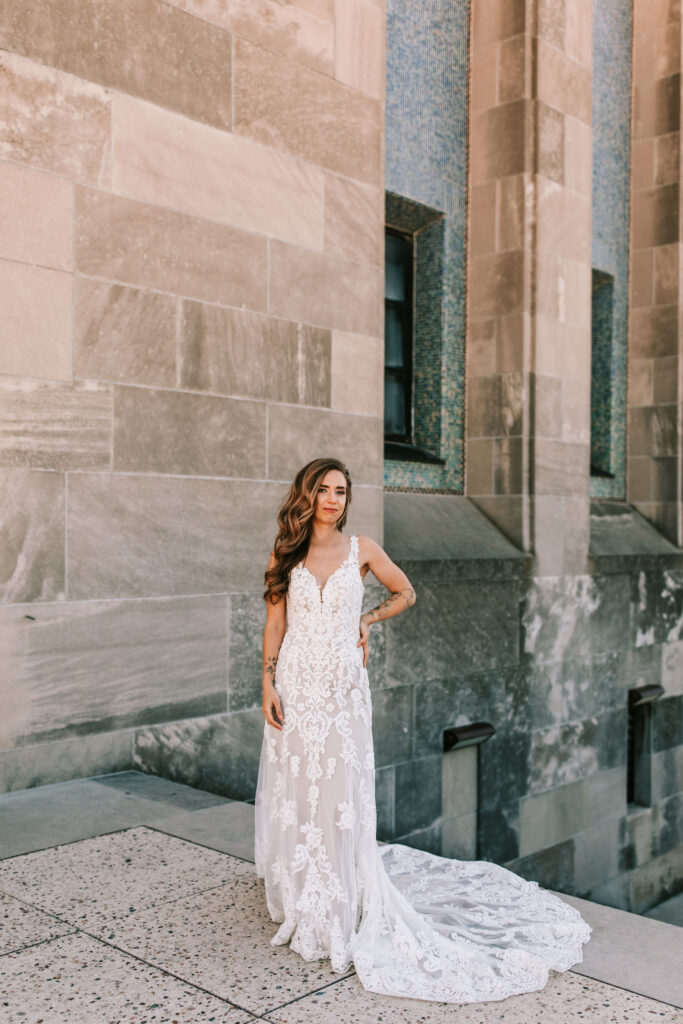 Bride in a spring season wedding long, lace wedding gown in front of a stone wall in Kansas City, Missouri photographed by Bailey Morris Photography.