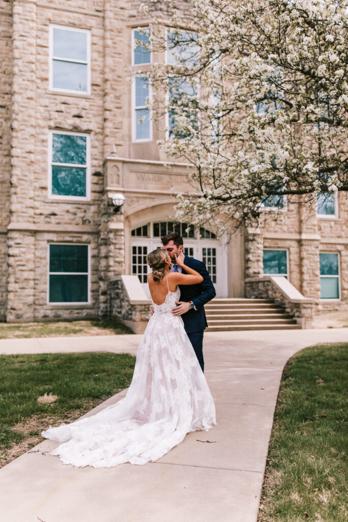 Bride and groom kissing in front of flowering trees during a spring season wedding in Ottawa, Kansas at the Fredrikson Center.