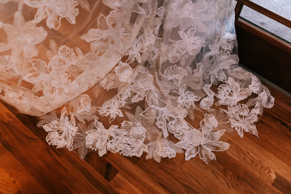 Lace gown flooding out over hardwood floor at a wedding venue in Ottowa, Kansas photographed by Bailey Morris photographer.