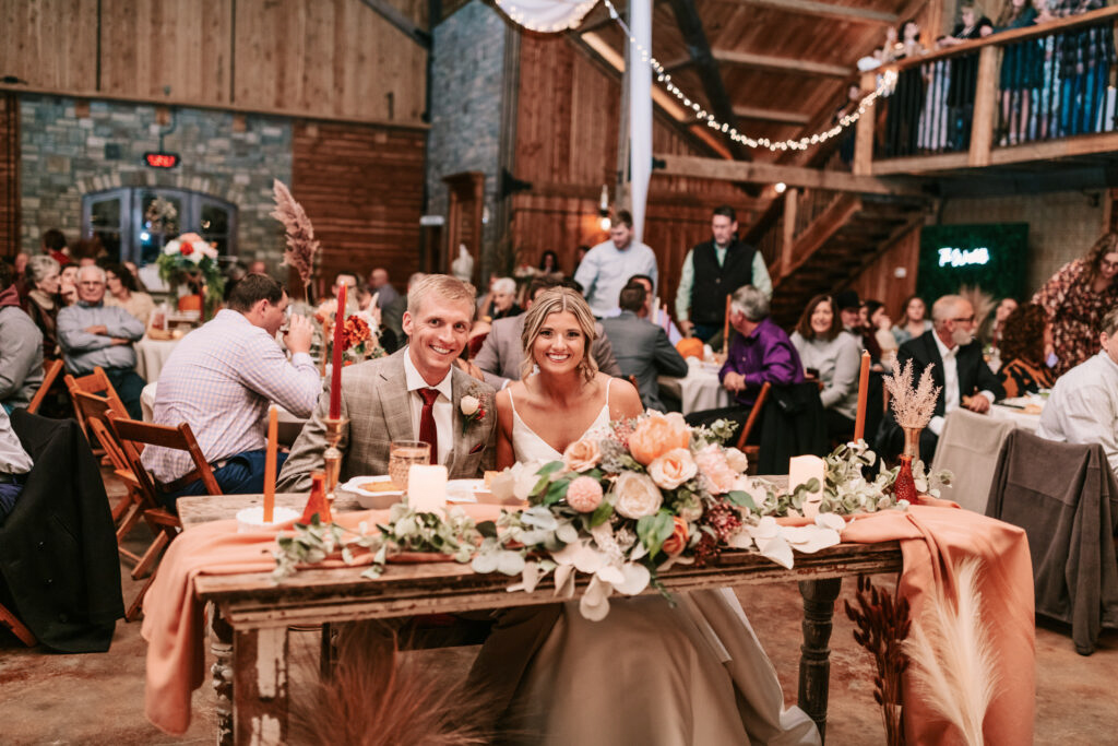 Bride and groom enjoying their head table at a wedding reception inside the spacious Mighty Oak Lodge in Lebanon Missouri. Wedding photography by Bailey Morris.