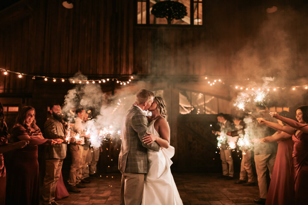 Bride and groom kissing at the end of the wedding reception, surrounded by friends and sparklers. 