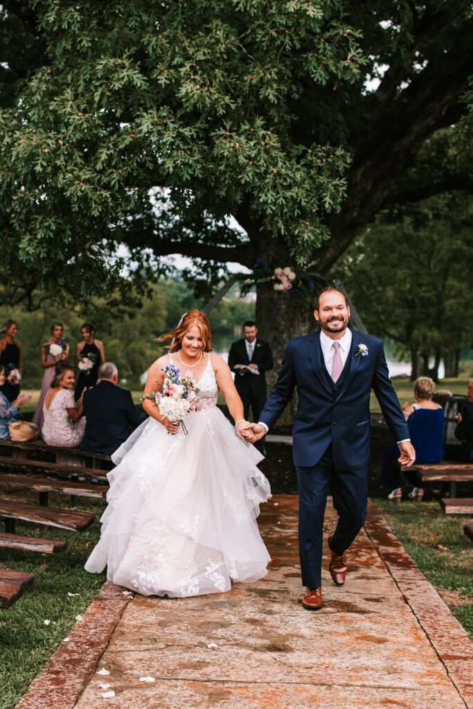 Husband and wife leaving their outdoor ceremony under the oak tree in Lebanon, Missouri. Walking up the path towards the barn. 