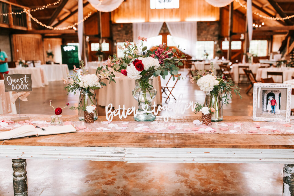 Decorate table with a sign that reads 'Better Together' in cursive surrounded by fresh florals in the reception space at Mighty Oak Lodge in Lebanon, Missouri. 