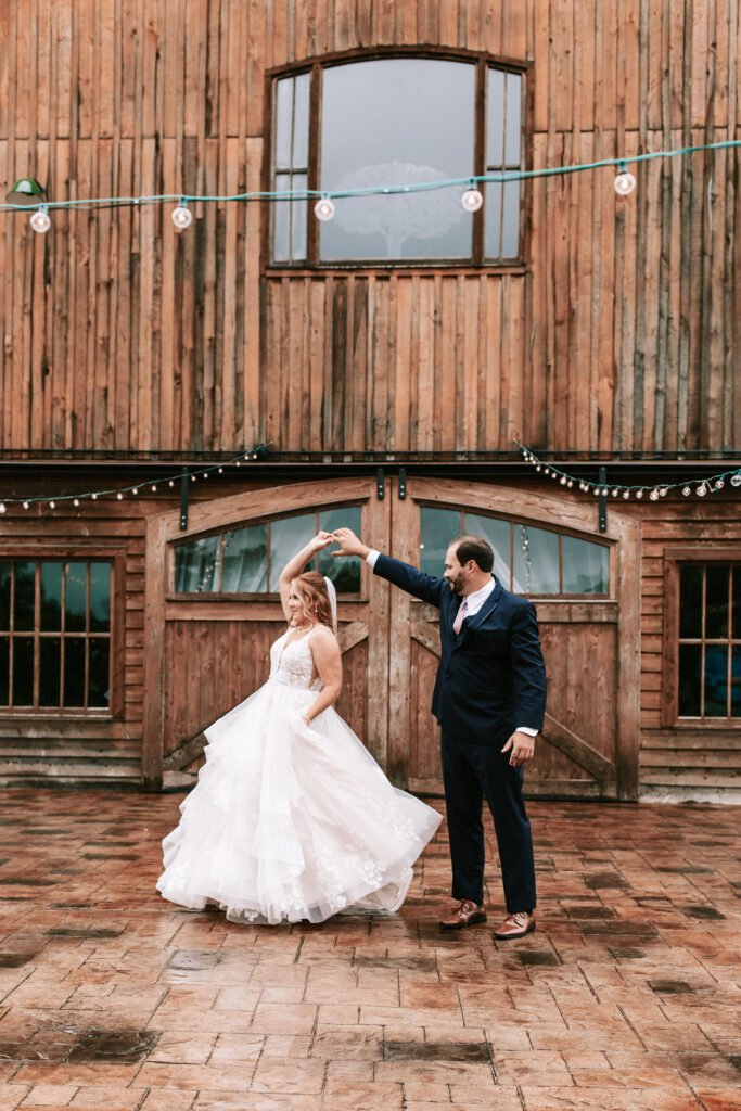 Groom twirling his bride on the outdoor patio space at their Lebanon, Missouri wedding venue. Wedding photography by Bailey Morris. 