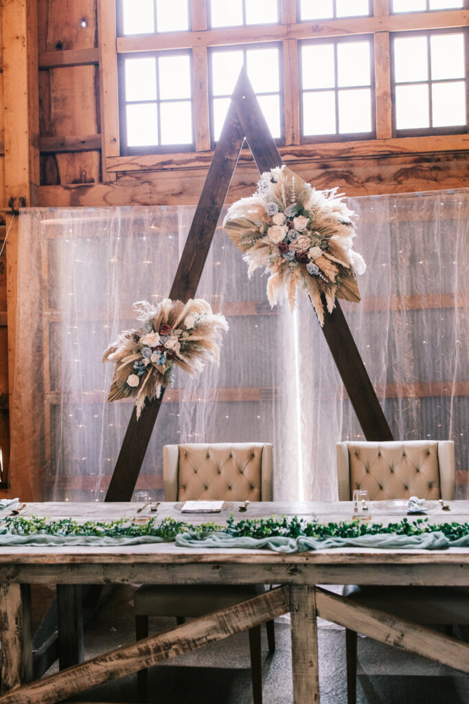 Wooden triangle backdrop adorned by spring flowers at a Missouri wedding reception photographed by Bailey Morris.
