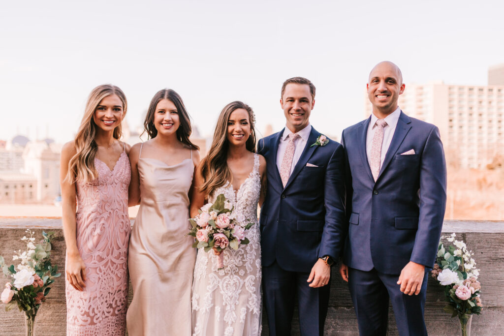 Spring wedding season rooftop wedding ceremony in Kansas City Missouri. Bride and groom with their wedding party in front of the Kansas City Skyline photographed by Bailey Morris Photography.
