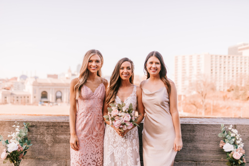 Bride and two bridesmaids standing in front of skyline at a rooftop wedding ceremony during the spring wedding season in Kansas City Missouri photographed by Bailey Morris.