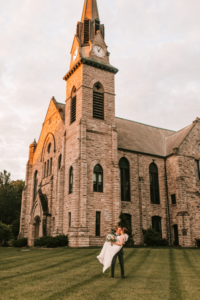 Groom carrying his bride in front of the chapel at Drury University in Springfield, Missouri photographed by Bailey Morris photographer.