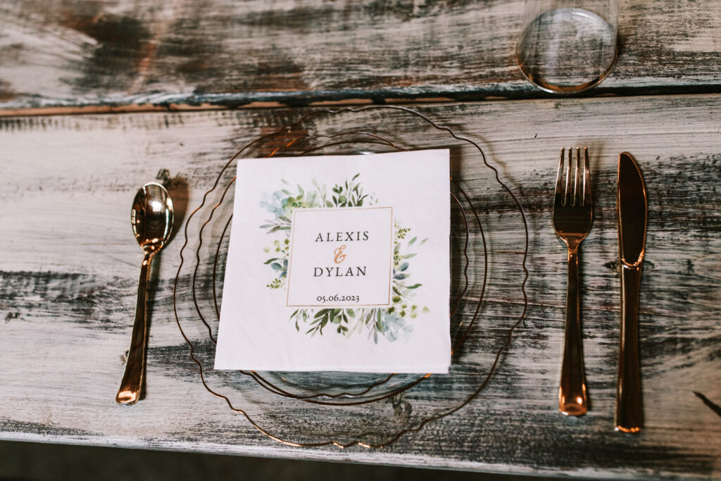 Spring season wedding stationary for Alexis and Dylan on a clear plate with gold trim on a gray, distressed wooden table photographed by Bailey Morris photography.