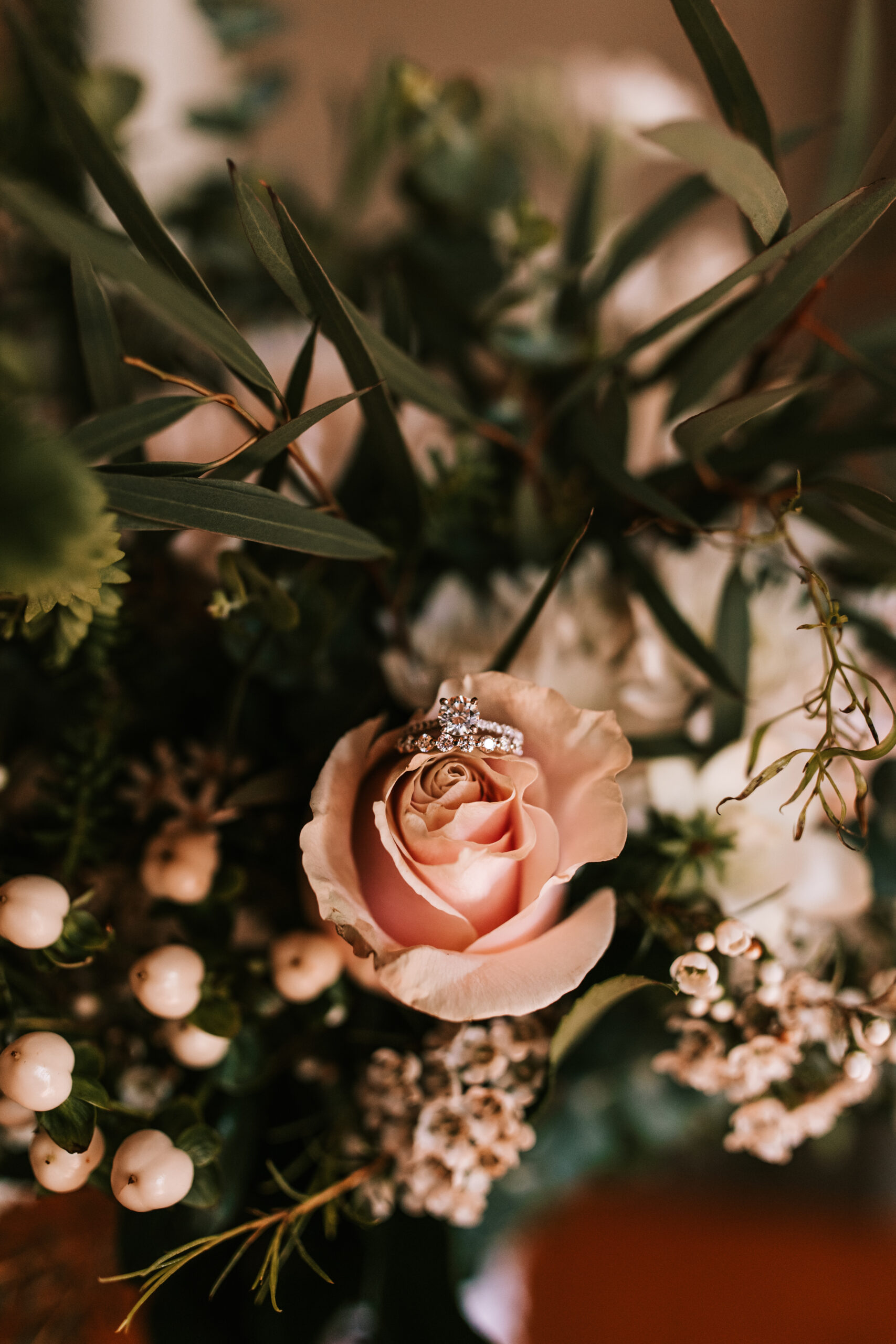 Diamond wedding ring resting on a peach rose in a bridal bouquet photographed by Bailey Morris Wedding Photography.