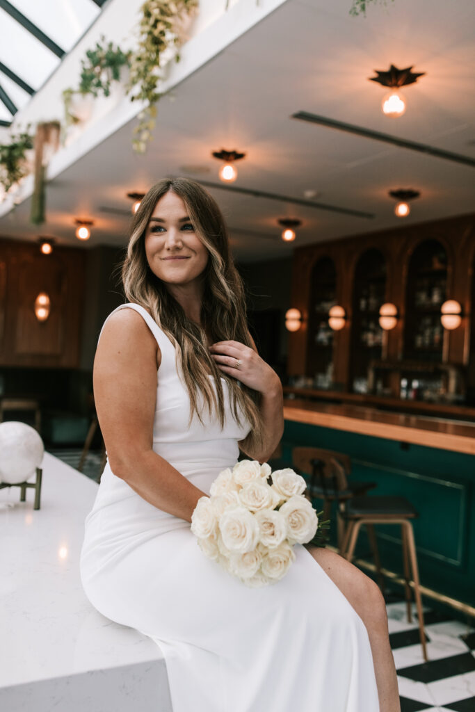 Bridal portrait in the conservatory after her Hotel Vandivort wedding. Bride is sitting on bar and holding her bridal bouquet of white roses. 