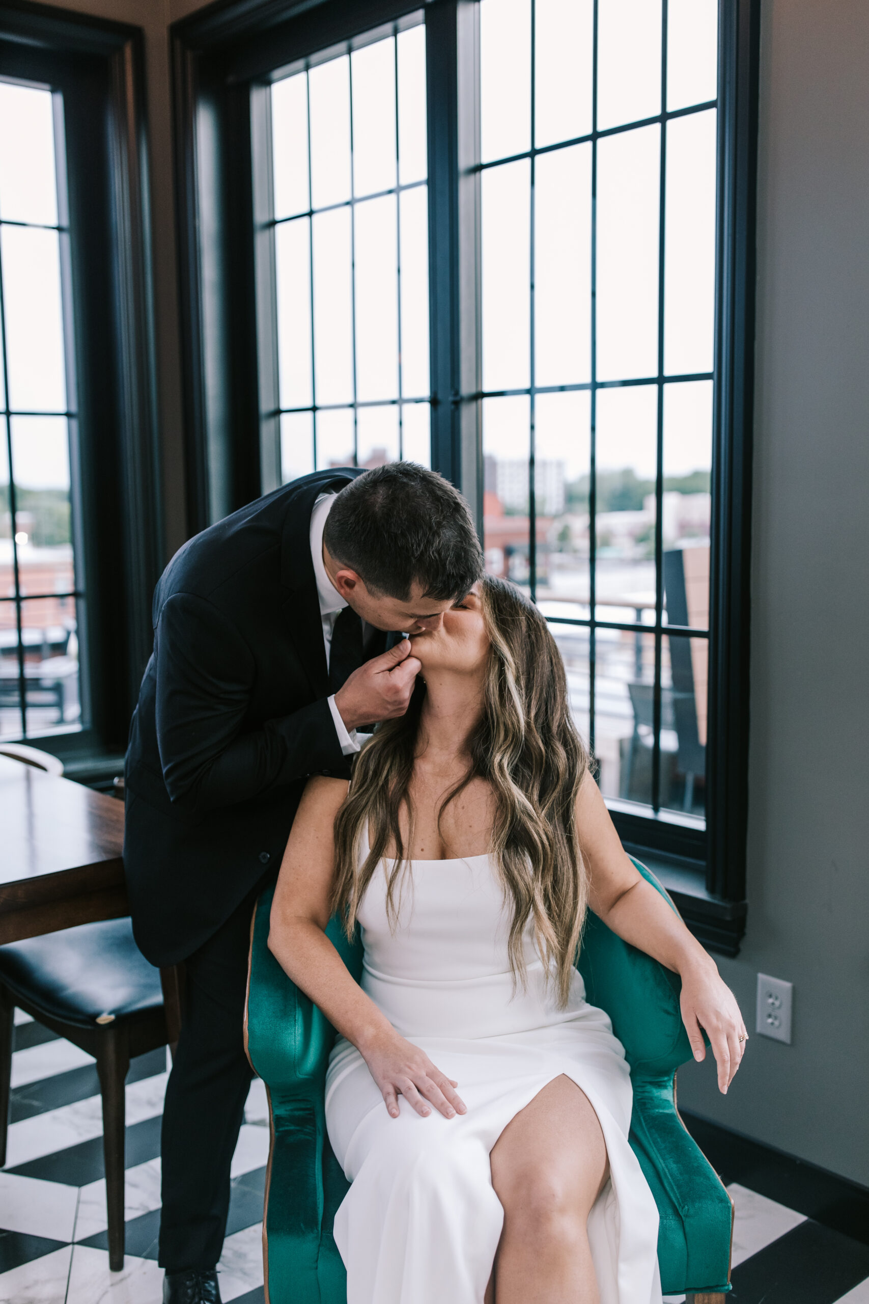 Groom kissing bride while she sits in a green velvet chair at a Hotel Vandivort Wedding. 