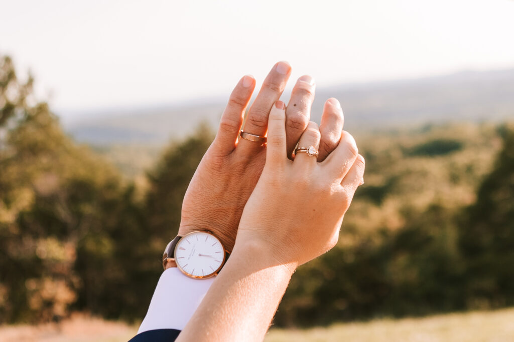 The groom and bride overlapping their left hands to show their wedding rings. Hands held up against the Branson landscape photographed by Bailey Morris Wedding Photography at The Atrium Wedding Venue.
