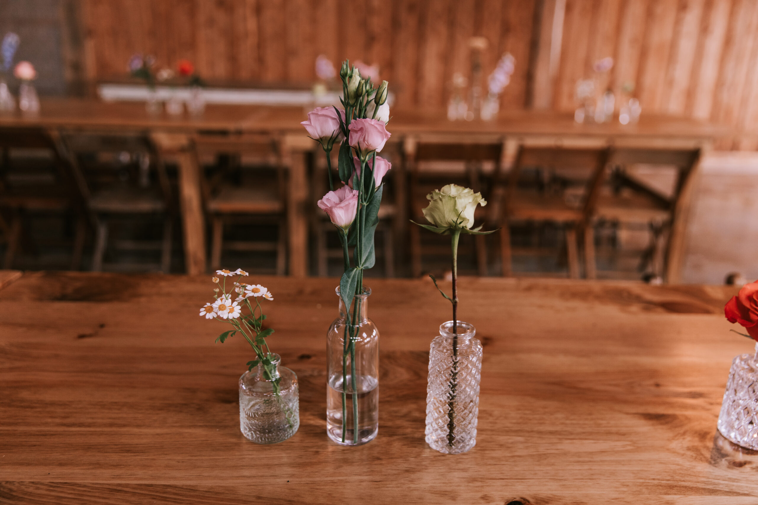 Three clear glass vases with summer flowers on the long tables inside MIghty Oak Lodge in Lebanon, Missouri. 
