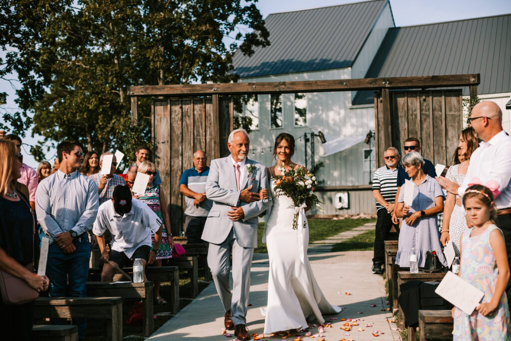 Father escorting the bride down the aisle at an outdoor ceremony at a Branson wedding venue: The Atrium. Photography by Bailey Morris wedding photographer.

