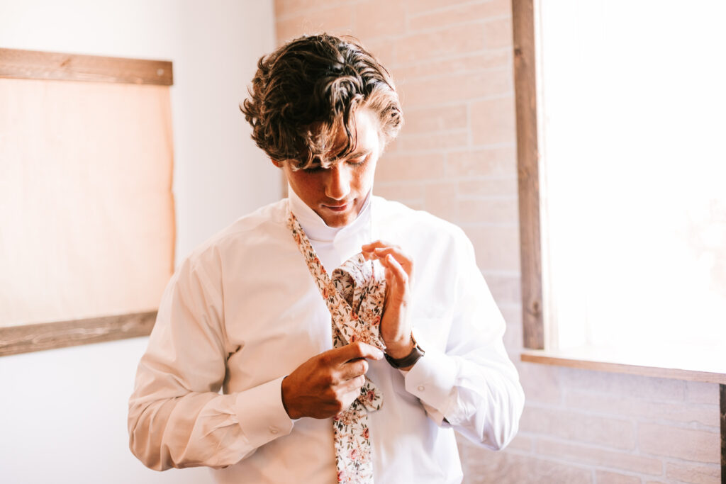 Groom getting ready and tying his tie at The Atrium Wedding Venue in Branson, Missouri. Photography by Bailey Morris.
