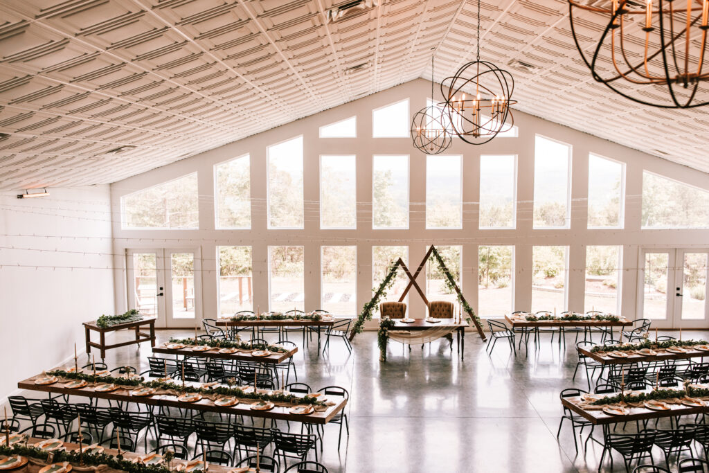 View from inside The Atrium Wedding Venue in Branson, Missouri looking out through multiple floor to ceiling windows over the Ozarks landscape. Tables are set up for a wedding reception.