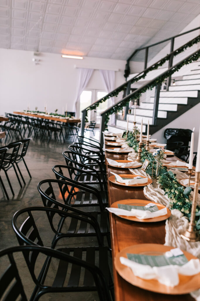 Wedding reception set up inside The Atrium in  Branson, Missouri. Black chairs and wooden tables against and a white staircase with black railing. 
