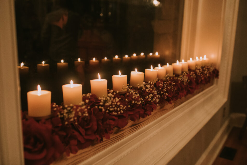 Row of candles in a windowsill at the mansion at Haseltine Estate wedding venue in springfield missouri. The candles are lit and surrounded by fresh red roses and babys breath.