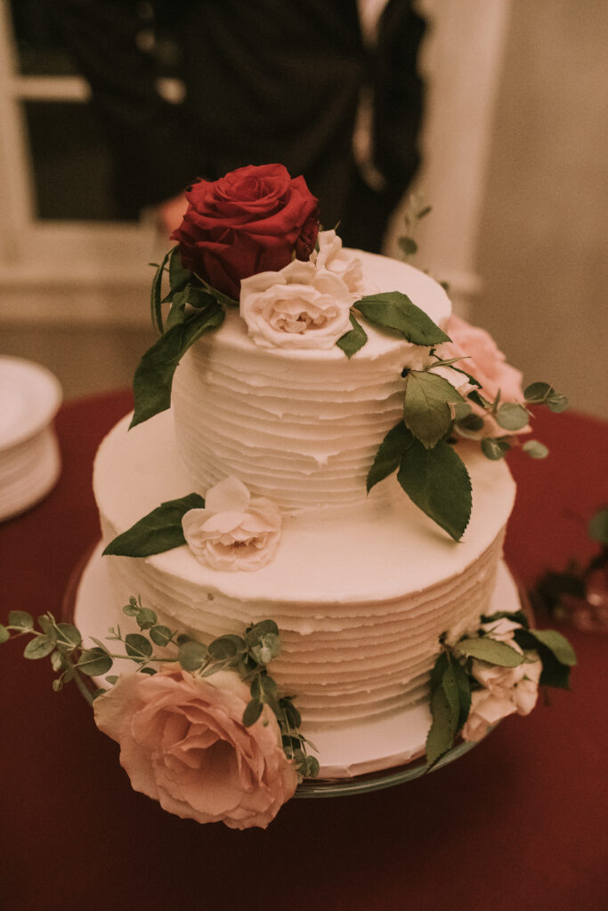 white wedding cake covered in fresh roses and greenery at the mansion at Haseltine Estate wedding venue in Springfield, Missouri.
