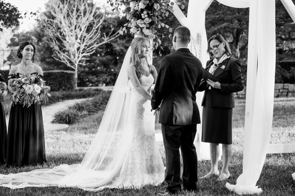 Black and white photo showing bride holding the hands of her groom and crying during the reading of her vows at Haseltine Estate wedding venue in Springfield Missouri.