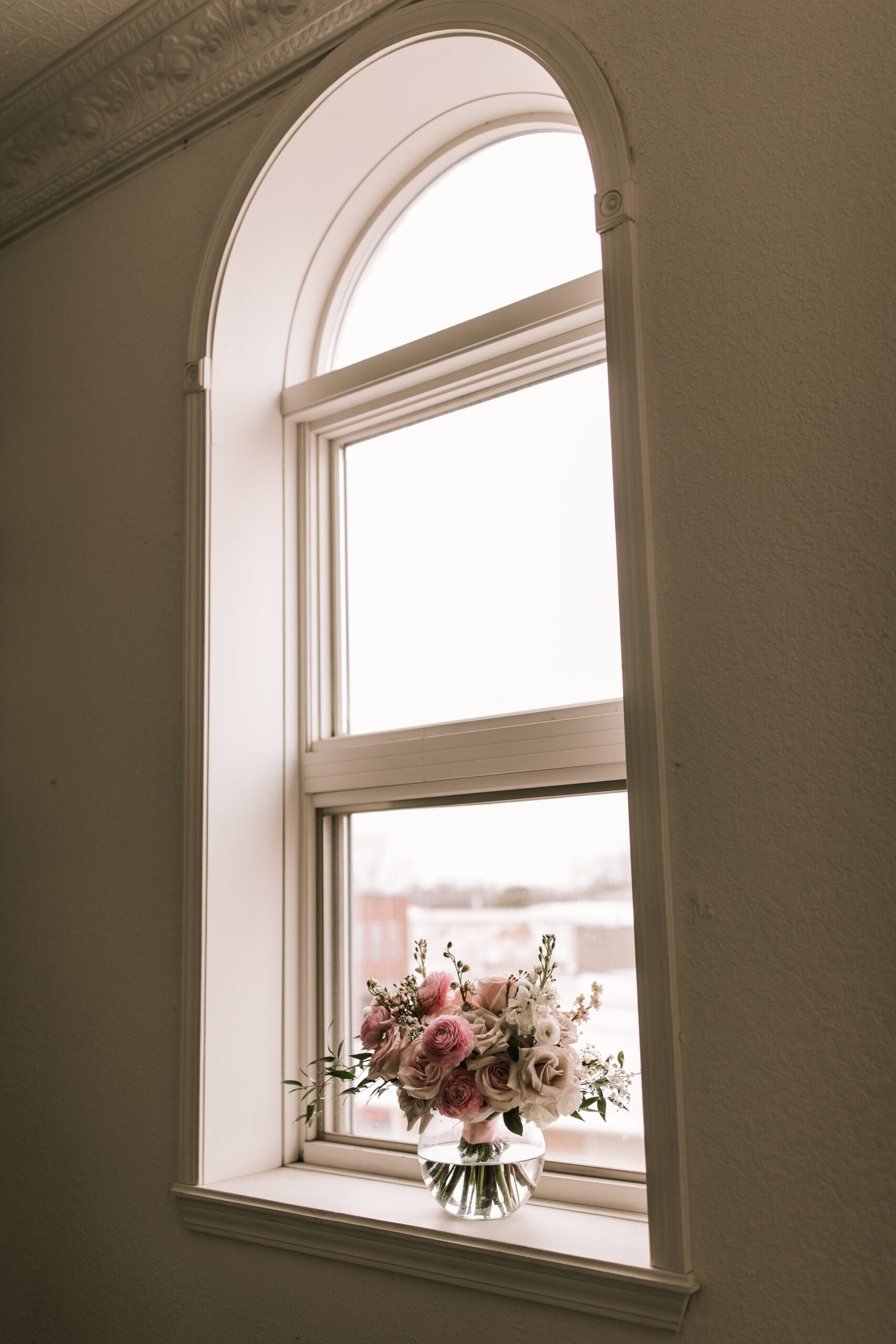 Pink and white rose Floral arrangement in a clear vase in a window sill at a Missouri Wedding Venue. Photography by Bailey Morris. 