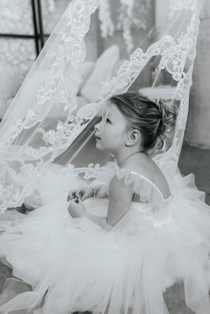 A flower girl peers up through the lace veil of the bride at a Missouri wedding. Black and white wedding photos by Bailey Morris.