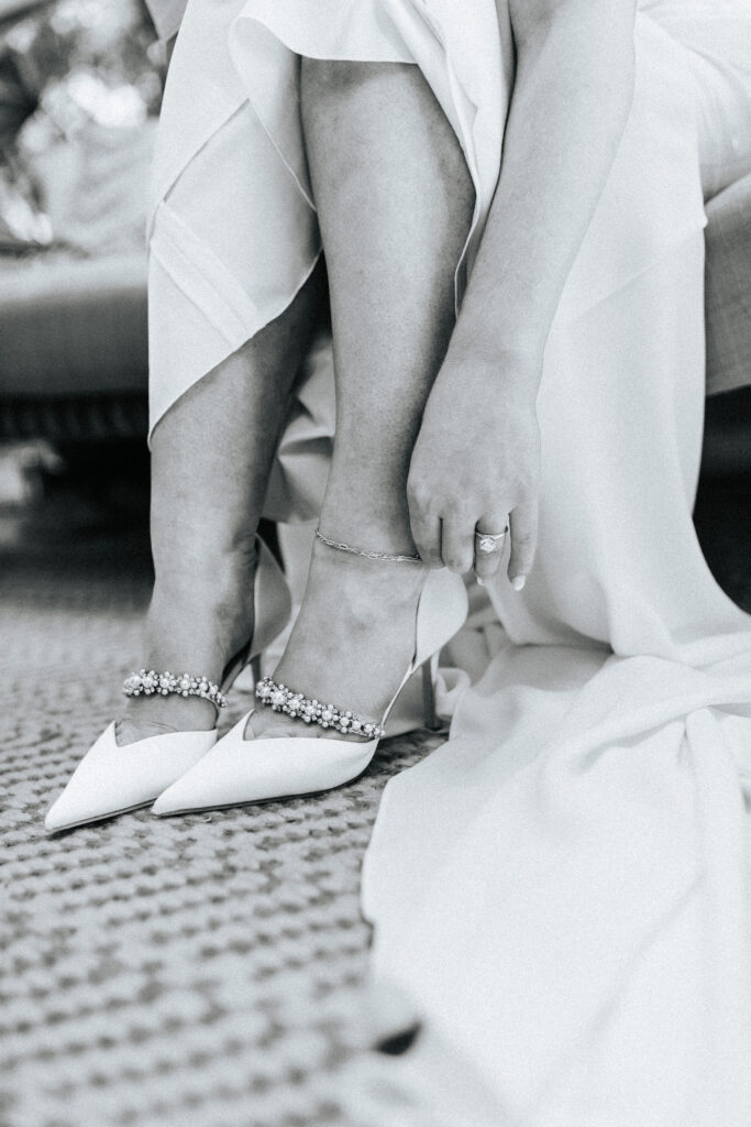 A bride is fastening the buckle on the ankle of her shoes at Finley Farms in Springfield, Missouri. Black and white wedding photos by Bailey Morris.