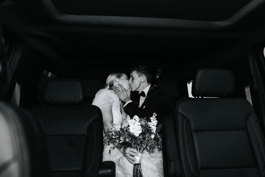 A bride and groom kiss in the back seat of a limo at their wedding in Lebanon, Missouri. Black and white wedding photos by Bailey Morris.