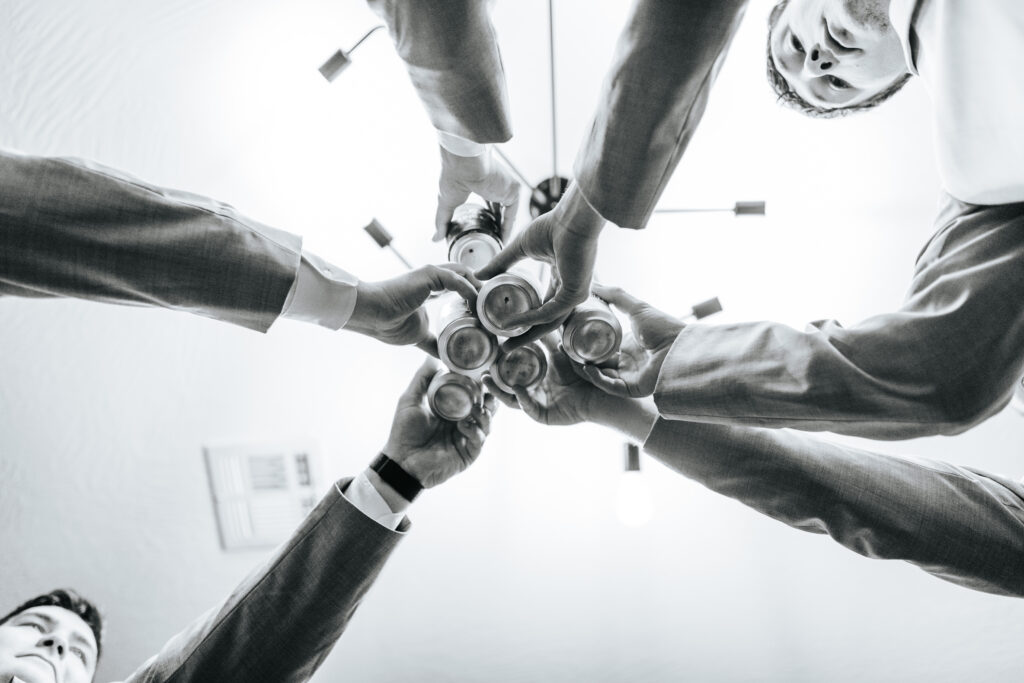 This shot taken from the floor shows the groom and his groomsmen meeting for a toast with their beer cans. Black and white wedding photos by Bailey Morris.