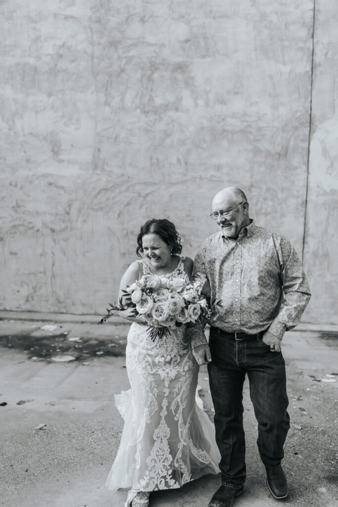 A bride and groom look down to the ground, smiling with joy at a Missouri wedding. Black and white wedding photos by Bailey Morris.