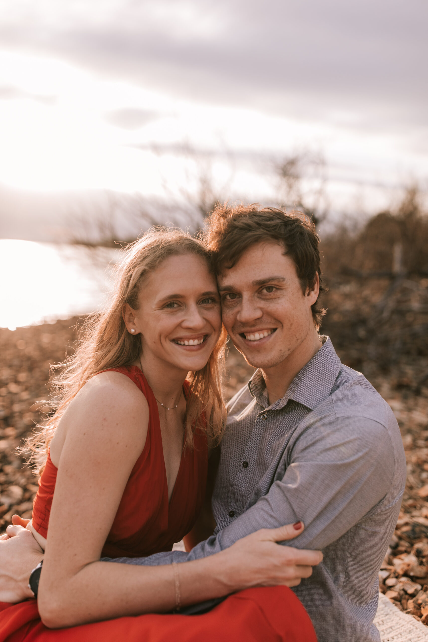 Engagement photo on a river bed in Missouri by Bailey Morris Photography. Bride is wearing a sleeveless, red, casual gown and groom is wearing a gray button down shirt.
