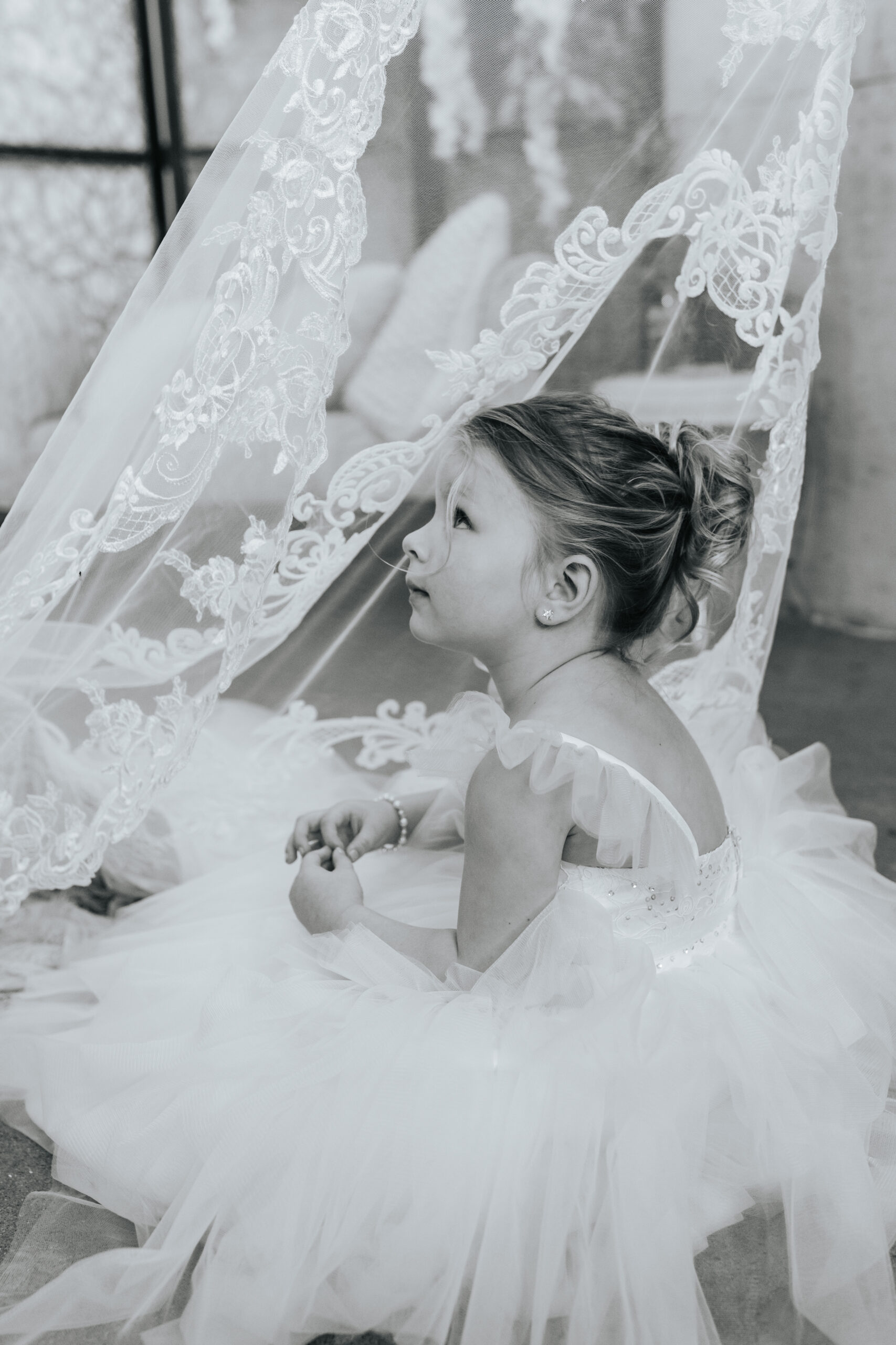 Flower girl peering up through white lace train of wedding gown. Photo from Missouri Wedding Photographer Bailey Morris.