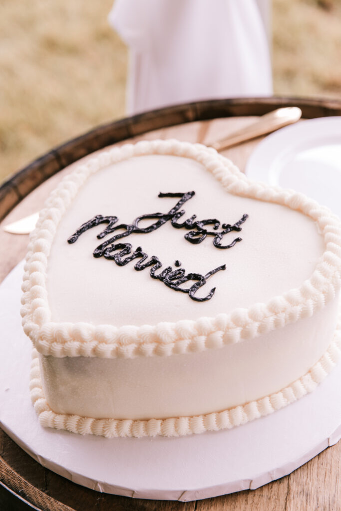 White heart shaped wedding cake piped with black letters that say 'Just Married' at a farm wedding. Bailey Morris Jefferson City Wedding Photographers