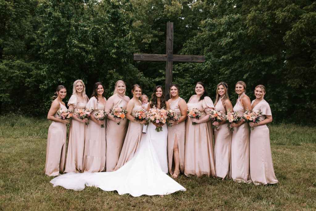 A bride and her bridal party in front of a wooden cross on a farm in Jefferson City, Missouri. Bailey Morris Wedding Photography. 