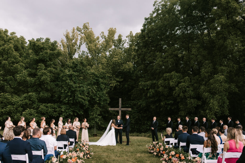 Wedding ceremony in front of dense woods on a farm in Jefferson City Missouri. Photo credit to Bailey Morris wedding photography. 
