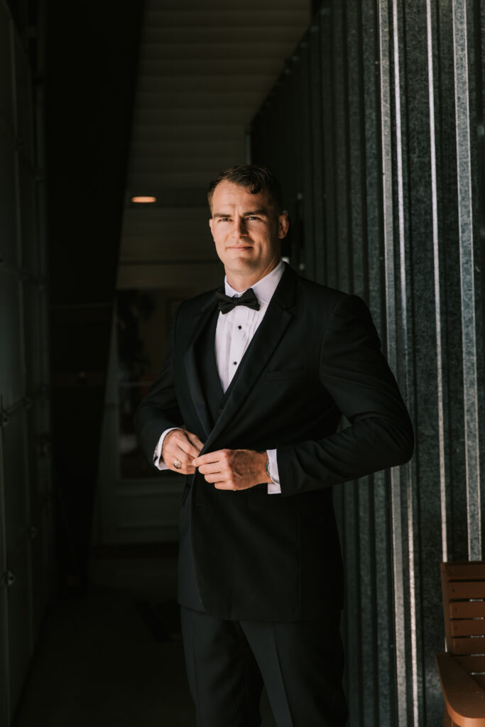 Groom buttoning his tuxedo jacket inside of a metal barn in Jefferson City Missouri. Photo by Bailey Morris wedding photography. 