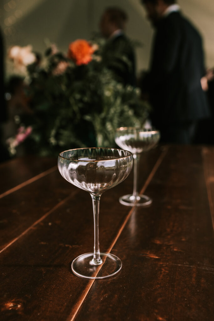 Two glasses on a dark wood bar with wedding florals in the background. Photo by Bailey Morris Jefferson City Wedding Photographers