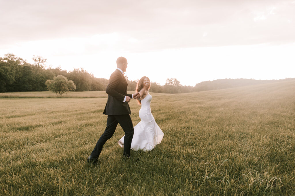 Bride and groom running through field. Photo by Bailey Morris Jefferson City Wedding Photographers.
