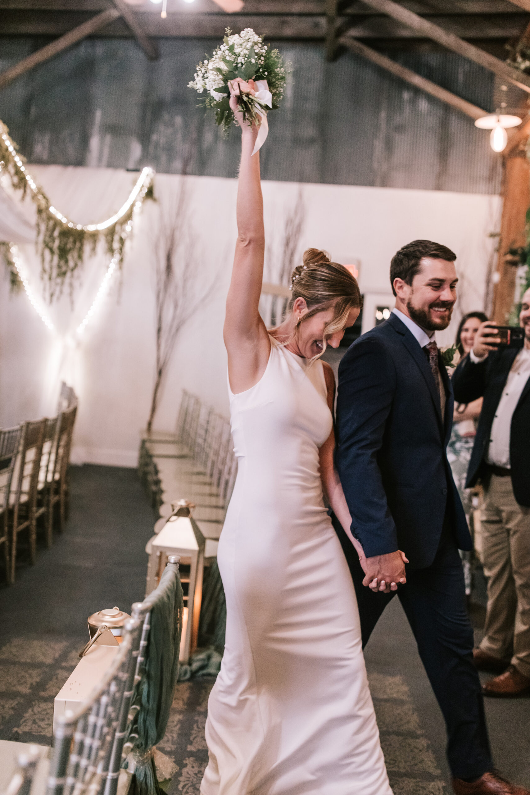 Bride extends her bouquet up in the air in accomplishment as she walks out of reception space at her wedding 