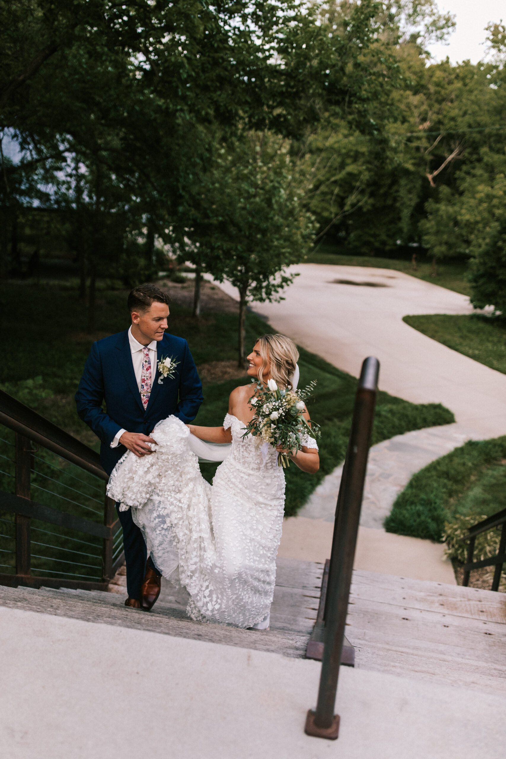 Groom holds the bride's train as they walk the grounds at Finley Farms.